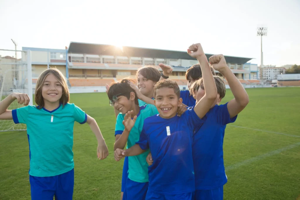 Seven-children-in-jerseys-celebrating-a-win-at-a-soccer-field