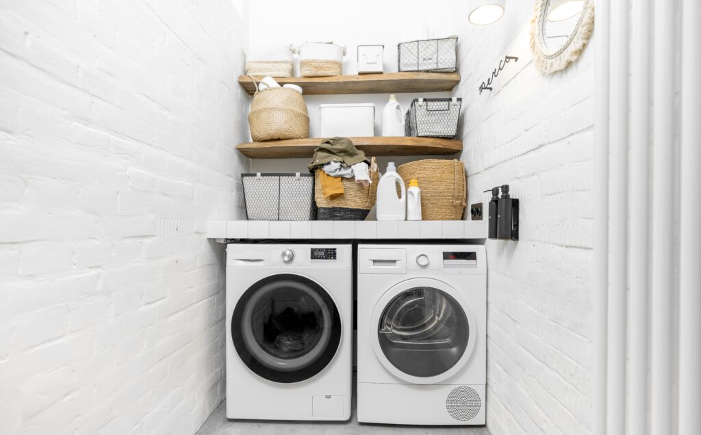 White laundry room with washing and drying machine and shelves with baskets above